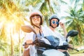 ÃÂ¡ouple travelers riding motorbike scooter in safety helmets during tropical vacation under palm trees